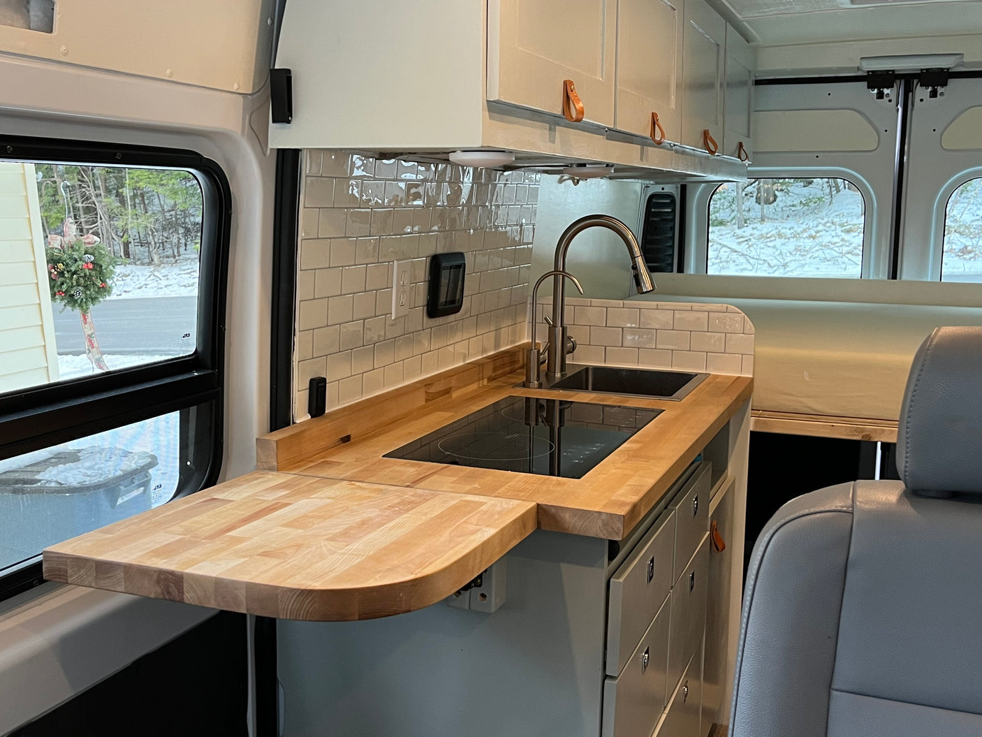 Stylish RV rental kitchen interior featuring wooden countertops, a sink, induction cooktop, subway tiles, and white cabinets.