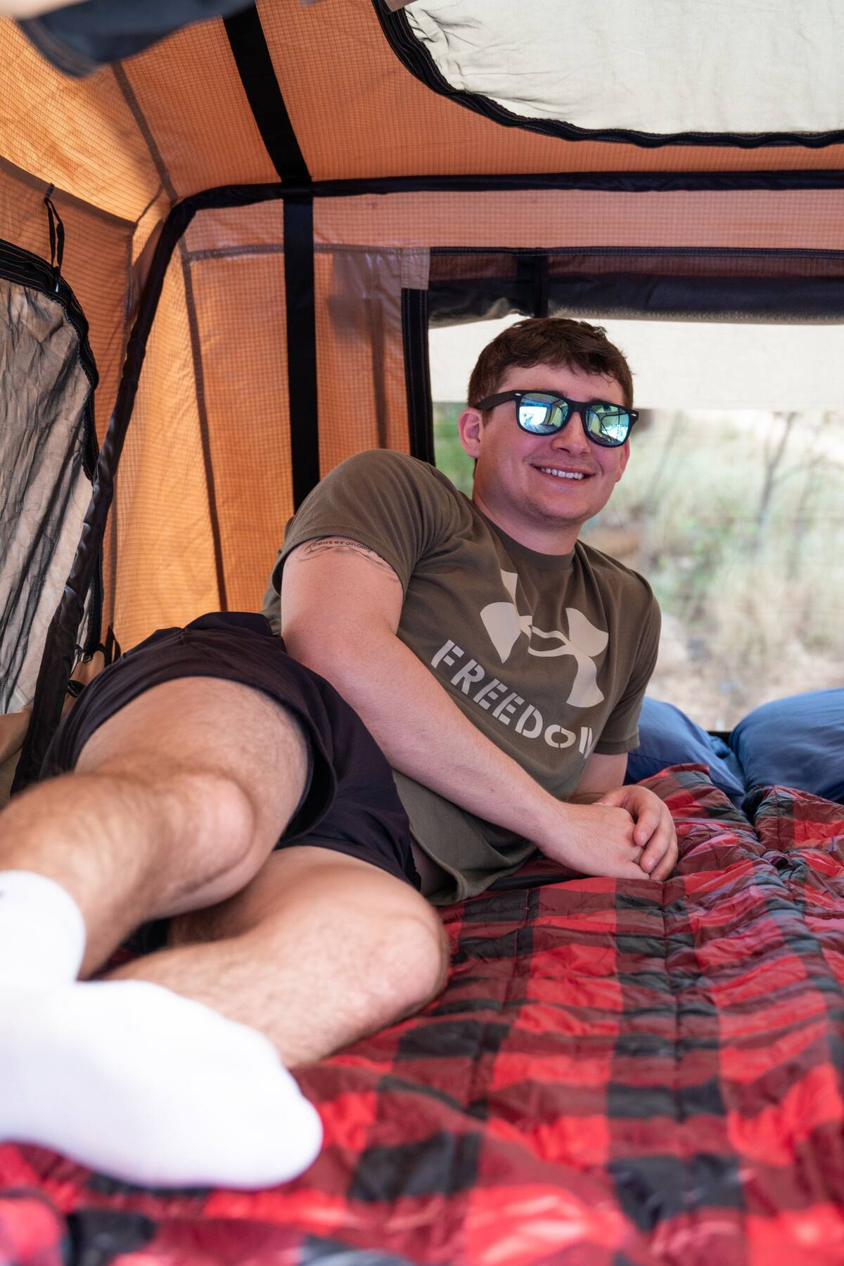 ready for an RV rental adventure.|Happy man relaxing inside an RV rental tent on a red plaid blanket
