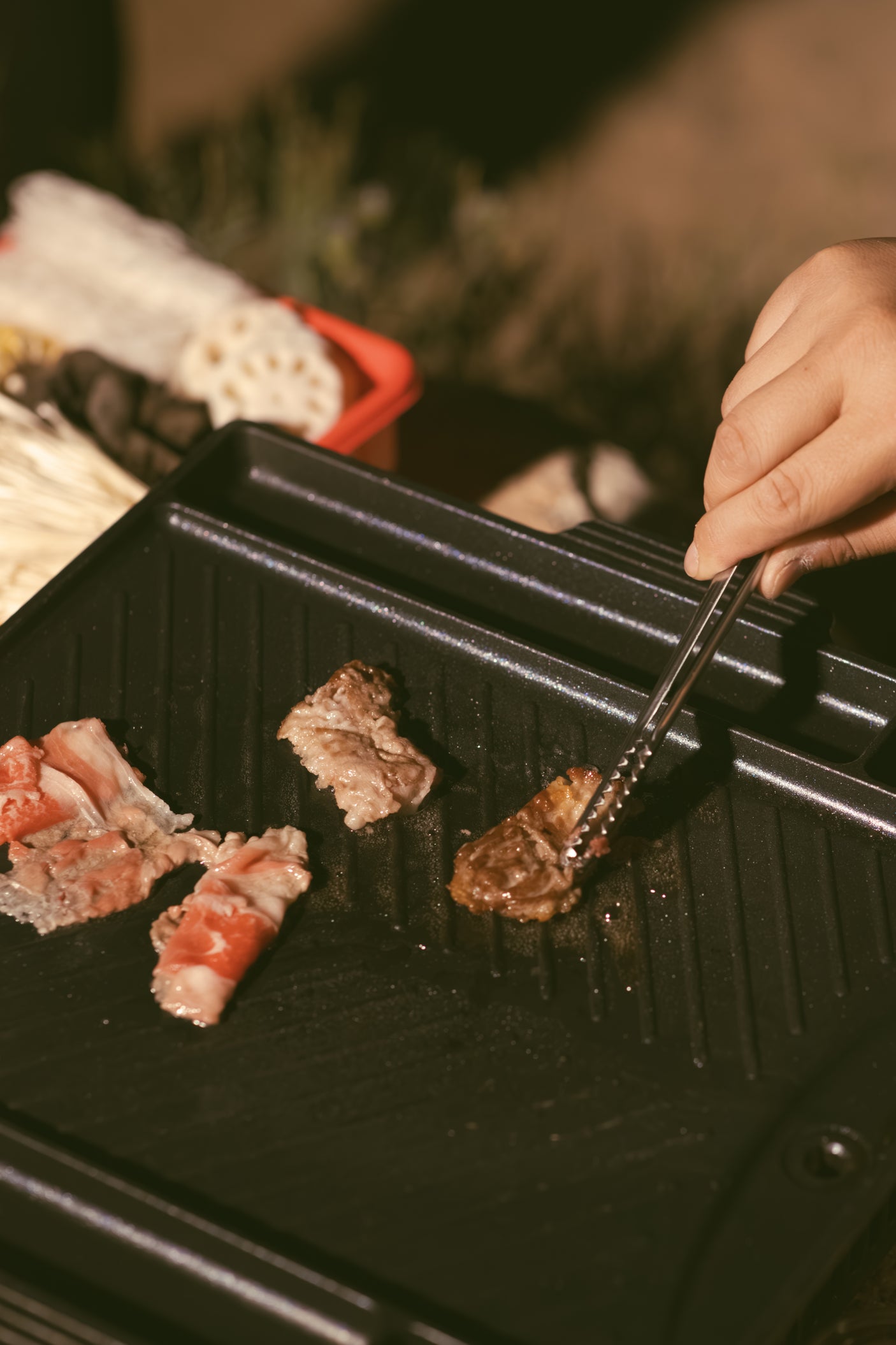 RV rental outdoor cooking: A hand uses tongs to flip meat on an electric grill, with raw ingredients in the background.
