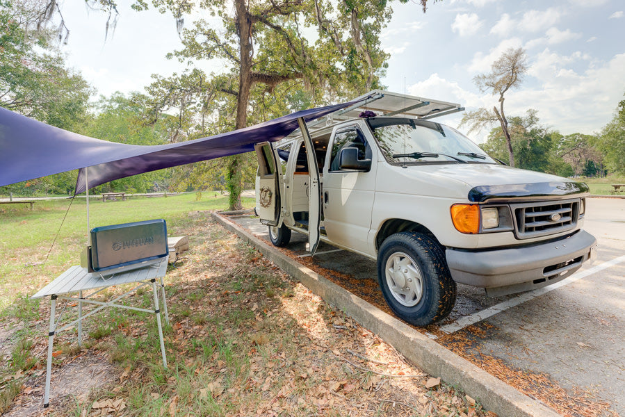 RV rental ready: white camper van with extended awning, roof solar panels, and outdoor table with power unit.