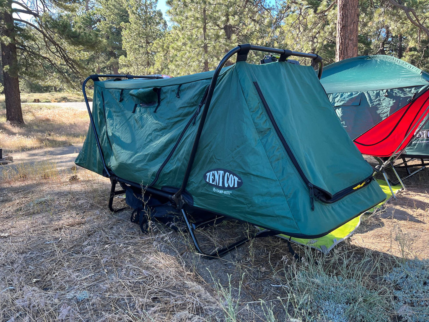 Two green Kamp-Rite Tent Cots set up in a sunny, wooded campsite. Perfect for flexible camping during your **RV rental** adventure.