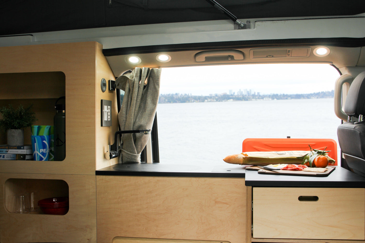 RV rental kitchen & scenic view. Wood cabinets, sink, food prep, and waterfront city skyline make for great van life.