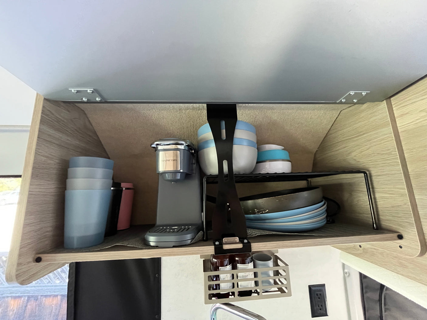 RV rental: Neatly organized overhead kitchen cabinet featuring a Minpresso coffee maker, dishes, and hanging storage.