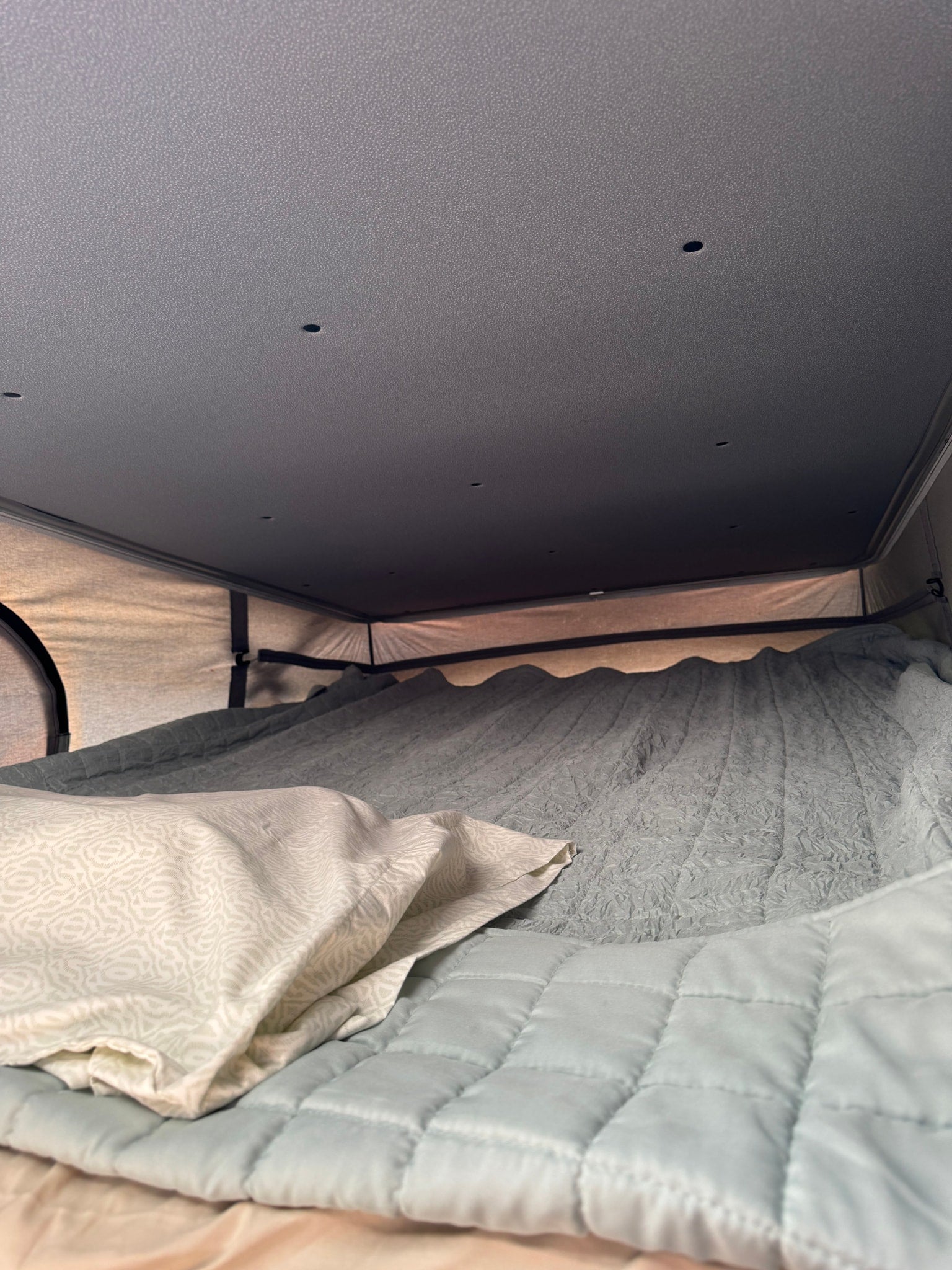 Inside an RV rental: a cozy bed with a patterned pillow, quilted blanket, and textured bedding under a ceiling with small lights.
