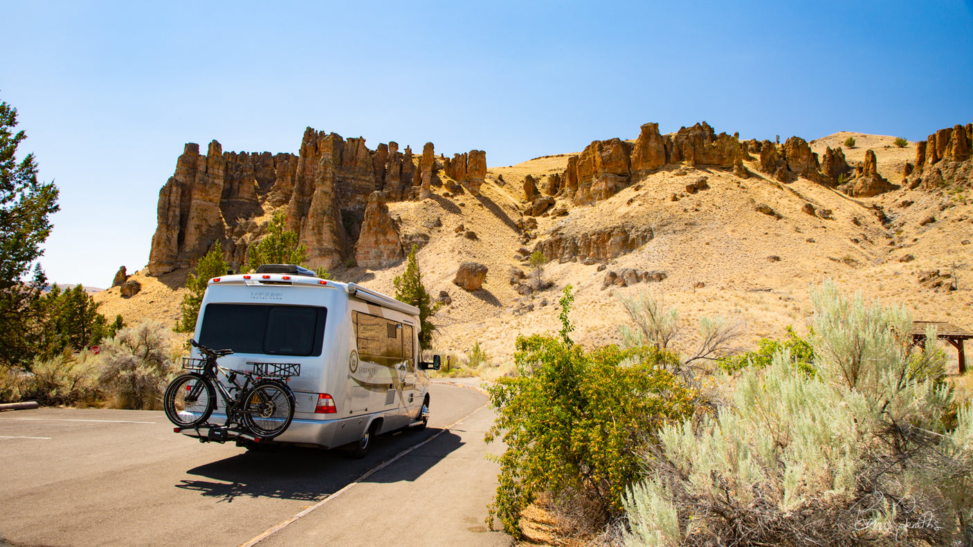 Silver RV rental with bikes parked amidst unique desert rock formations. Perfect for a scenic road trip adventure.