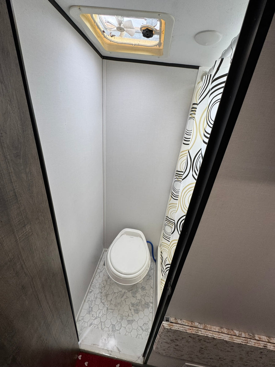 parked outdoors under trees.|A white and brown Retro Riverside RV rental with its door open