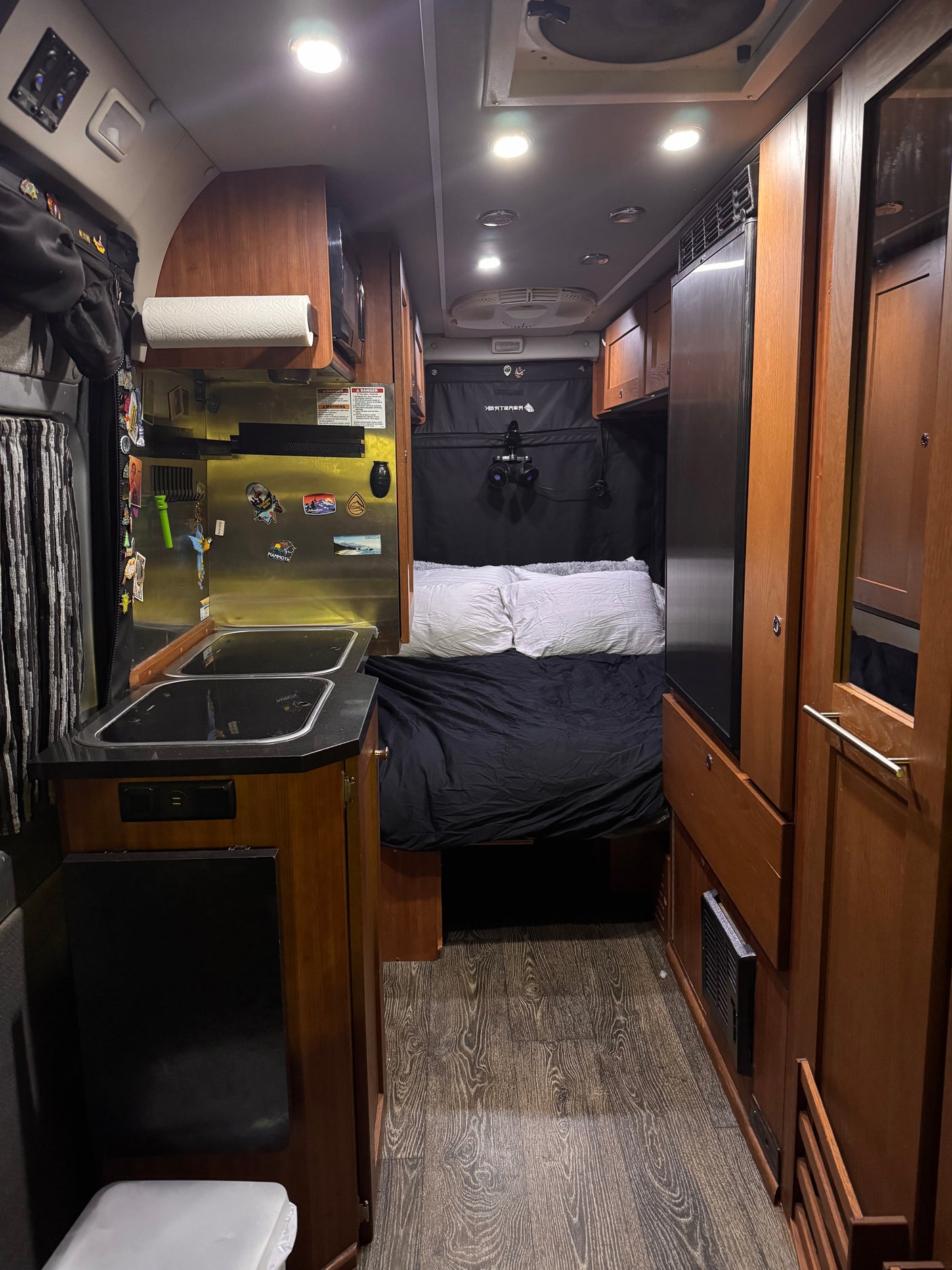 Discover this cozy RV rental's interior! Features a compact kitchen, comfortable bed, and warm wood accents.