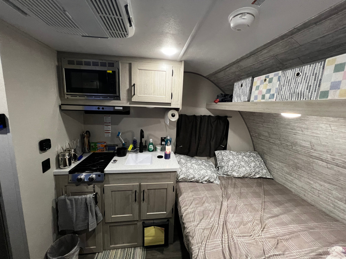 RV rental interior featuring a compact kitchen, comfortable bed, and convenient overhead storage bins.