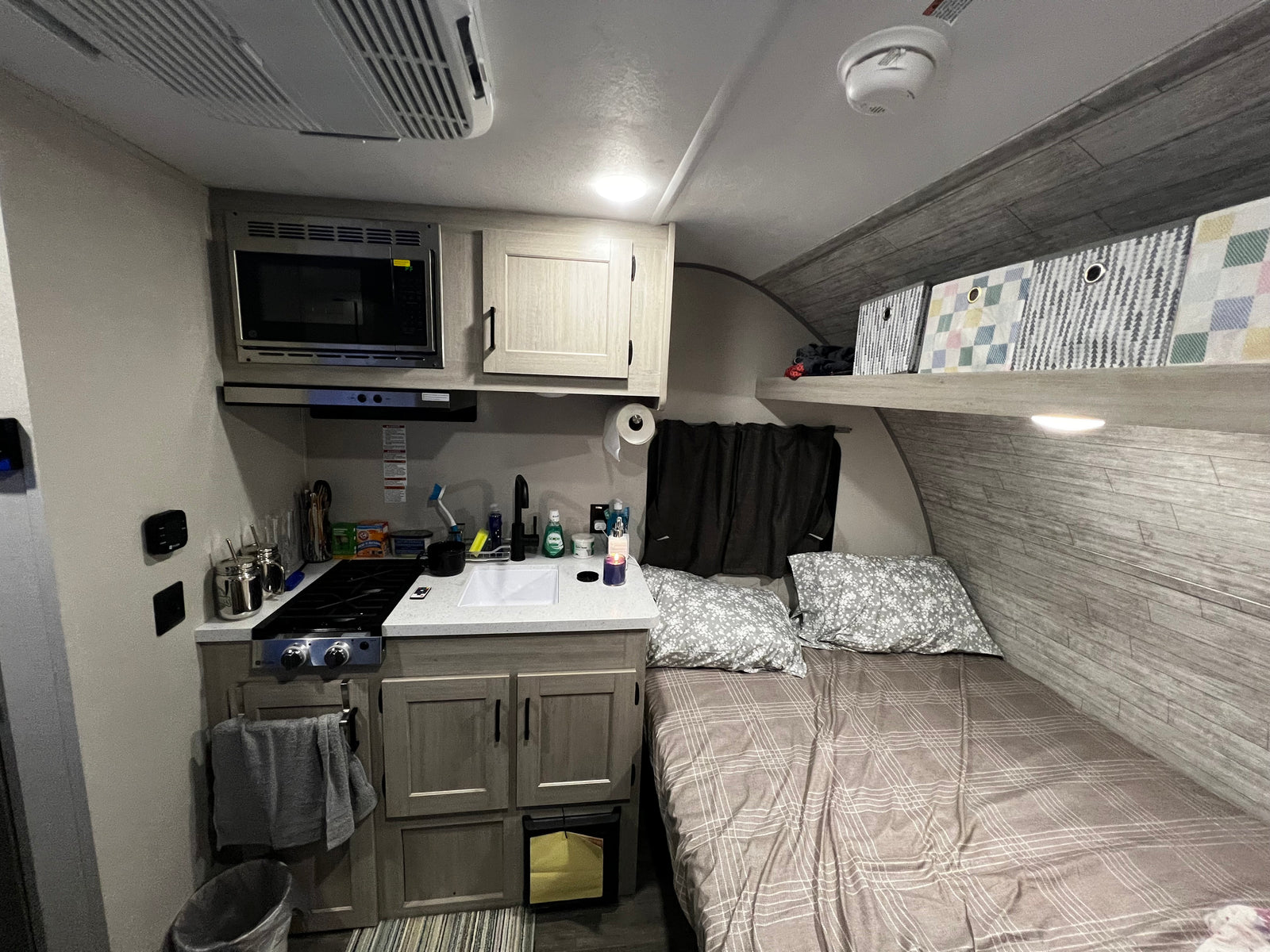 RV rental interior featuring a compact kitchen, comfortable bed, and convenient overhead storage bins.