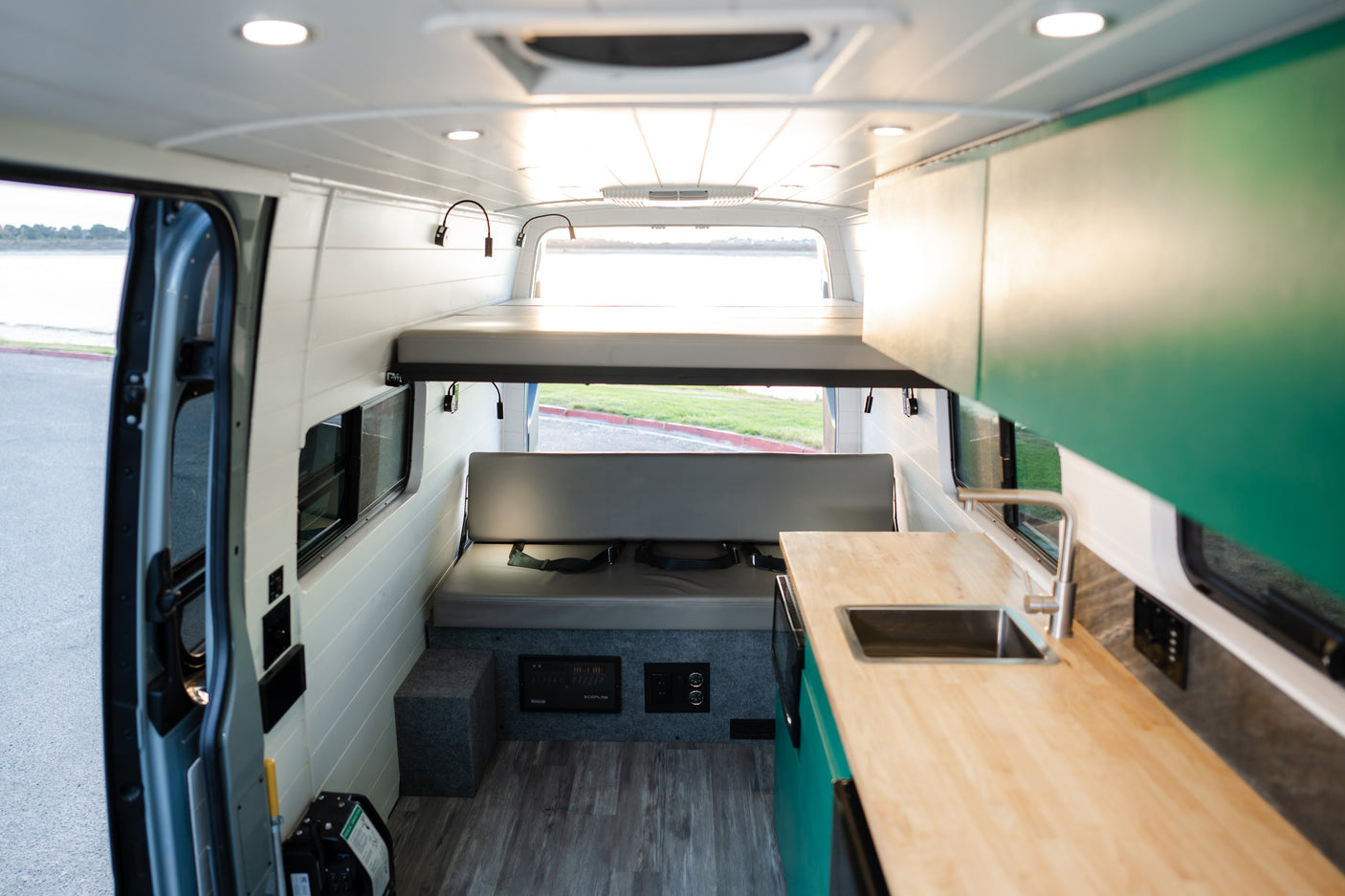 Bright RV rental interior with elevated bed, seating bench, and kitchen counter with sink, ideal for adventurous road trips.