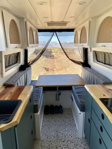 Inside a stylish rv rental, showing a cozy camper van interior with bench seating, kitchen, and panoramic canyon views.