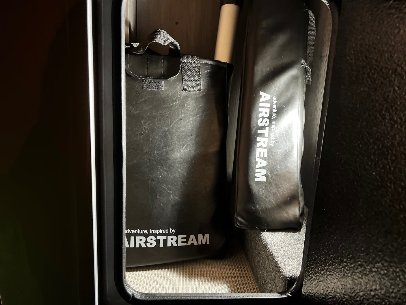 Airstream-branded black bags and gear neatly stored within an RV rental compartment.