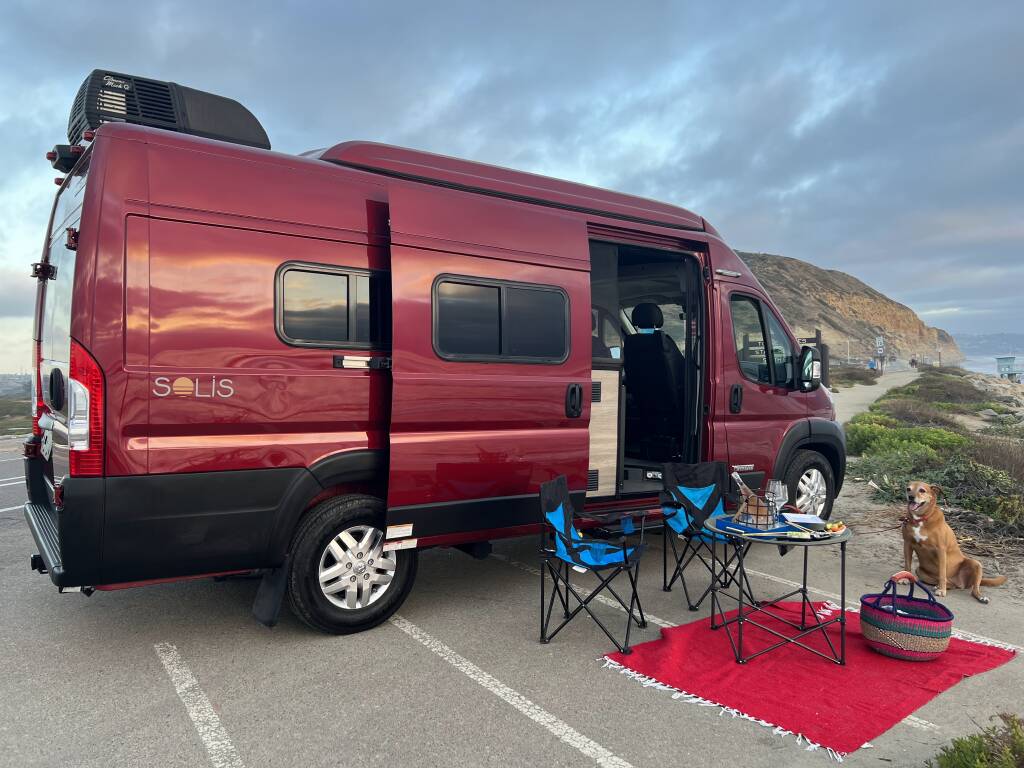 parked outdoors with its pop-top raised.|Red rv rental parked seaside with a dog