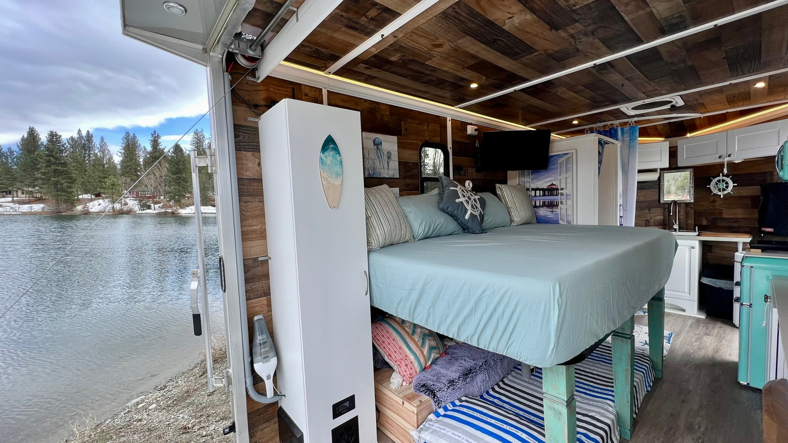 Unique RV rental interior: elevated bed, kitchen, and stunning lake views from the open ramp. Your cozy glamping retreat.