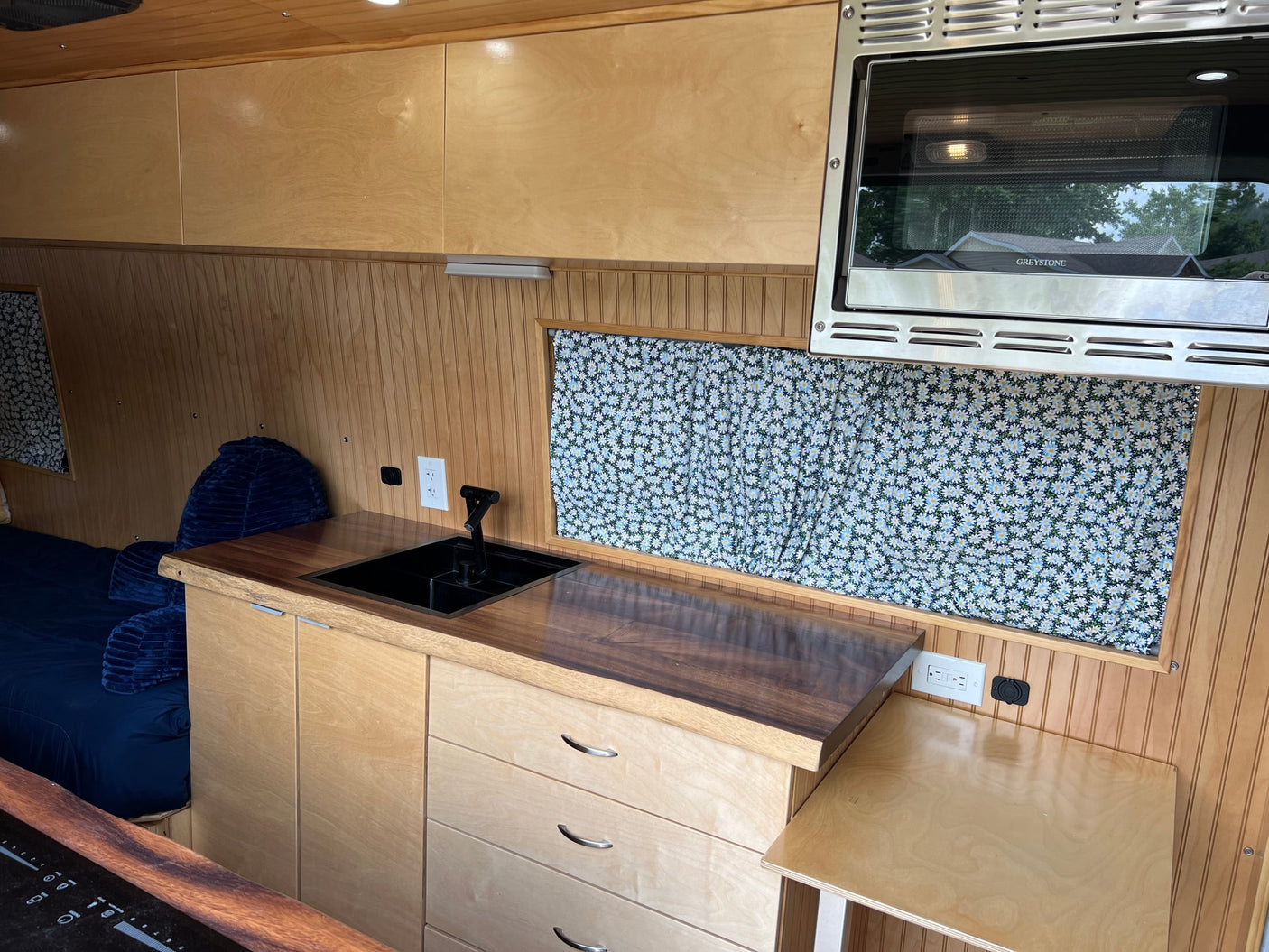 Compact RV rental interior featuring a practical kitchen with sink, microwave, wood cabinetry, and comfortable bed area.