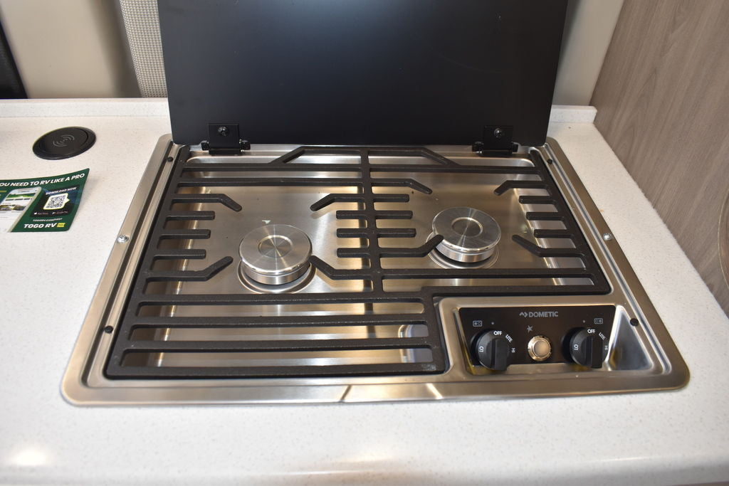 RV rental kitchen features a Dometic two-burner stovetop with grates and control knobs, lid open.