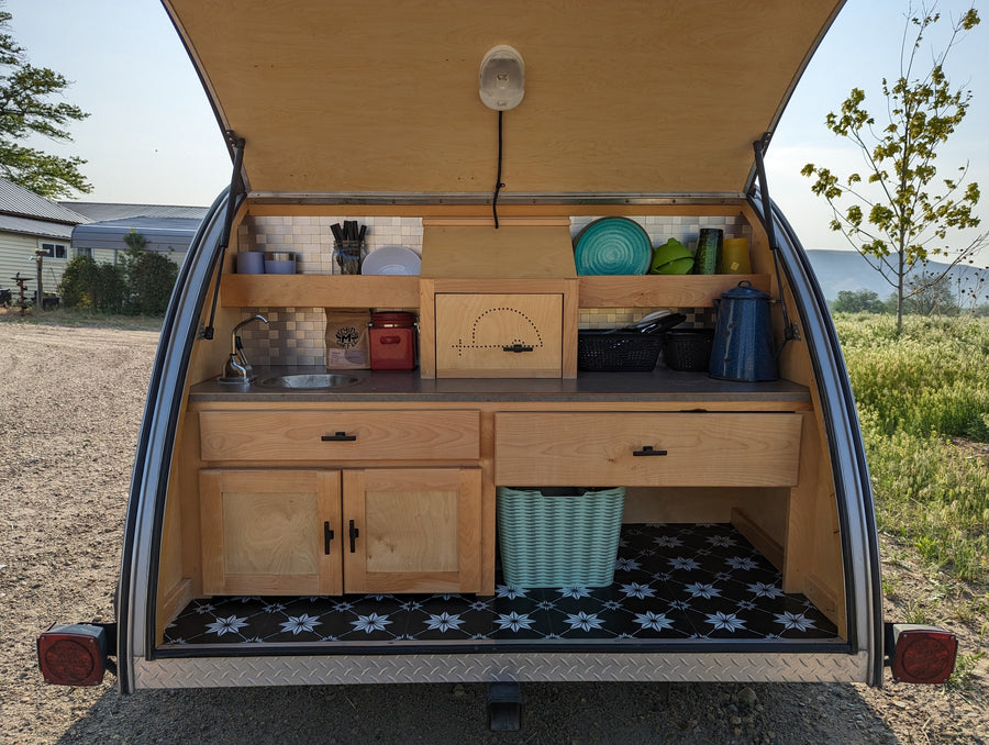 Compact rv rental teardrop camper kitchen featuring a sink, wooden cabinetry, tiled backsplash, and patterned floor.