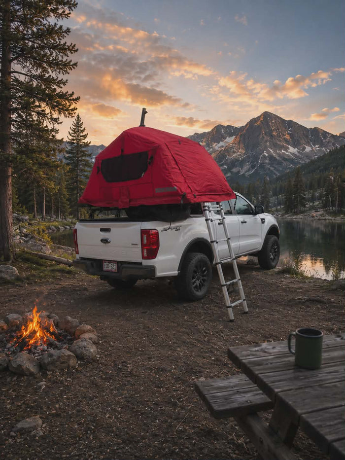 and majestic mountains by a lake. Perfect rv rental setup.|RV rental pickup truck with a roof-top tent overlooks a scenic mountain lake and snowy peaks. Ideal for outdoor adventures.|Adventure awaits with this RV rental alternative: a white truck featuring a red rooftop tent