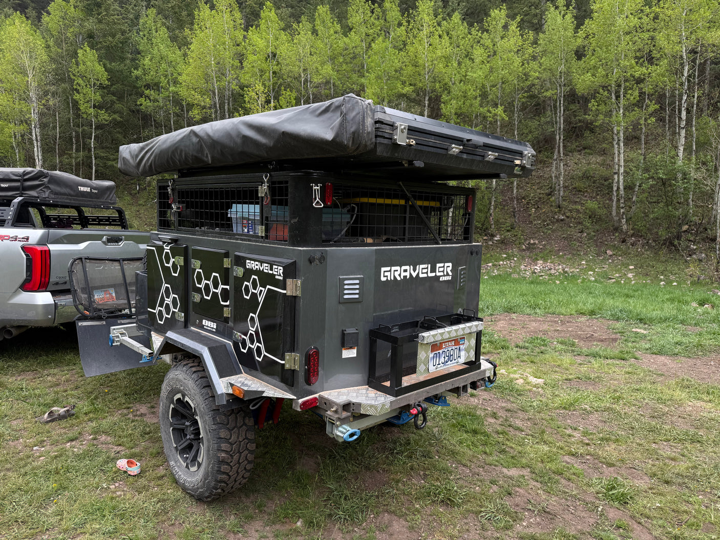 Adventure-ready overland trailer **RV rental** for camping, equipped with a rooftop tent, parked in a lush forest.
