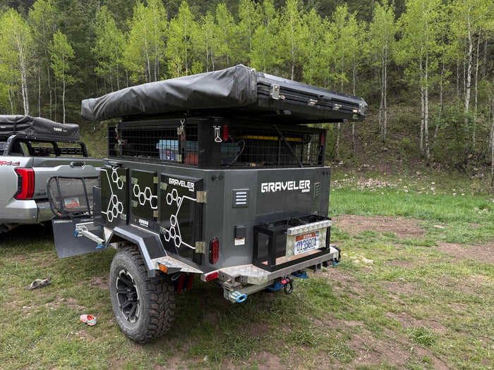 Adventure-ready overland trailer **RV rental** for camping, equipped with a rooftop tent, parked in a lush forest.