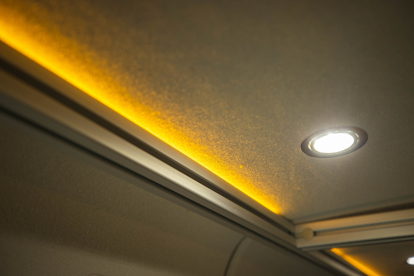 Cozy RV rental interior with warm accent strip lighting and bright spot light on a textured ceiling.