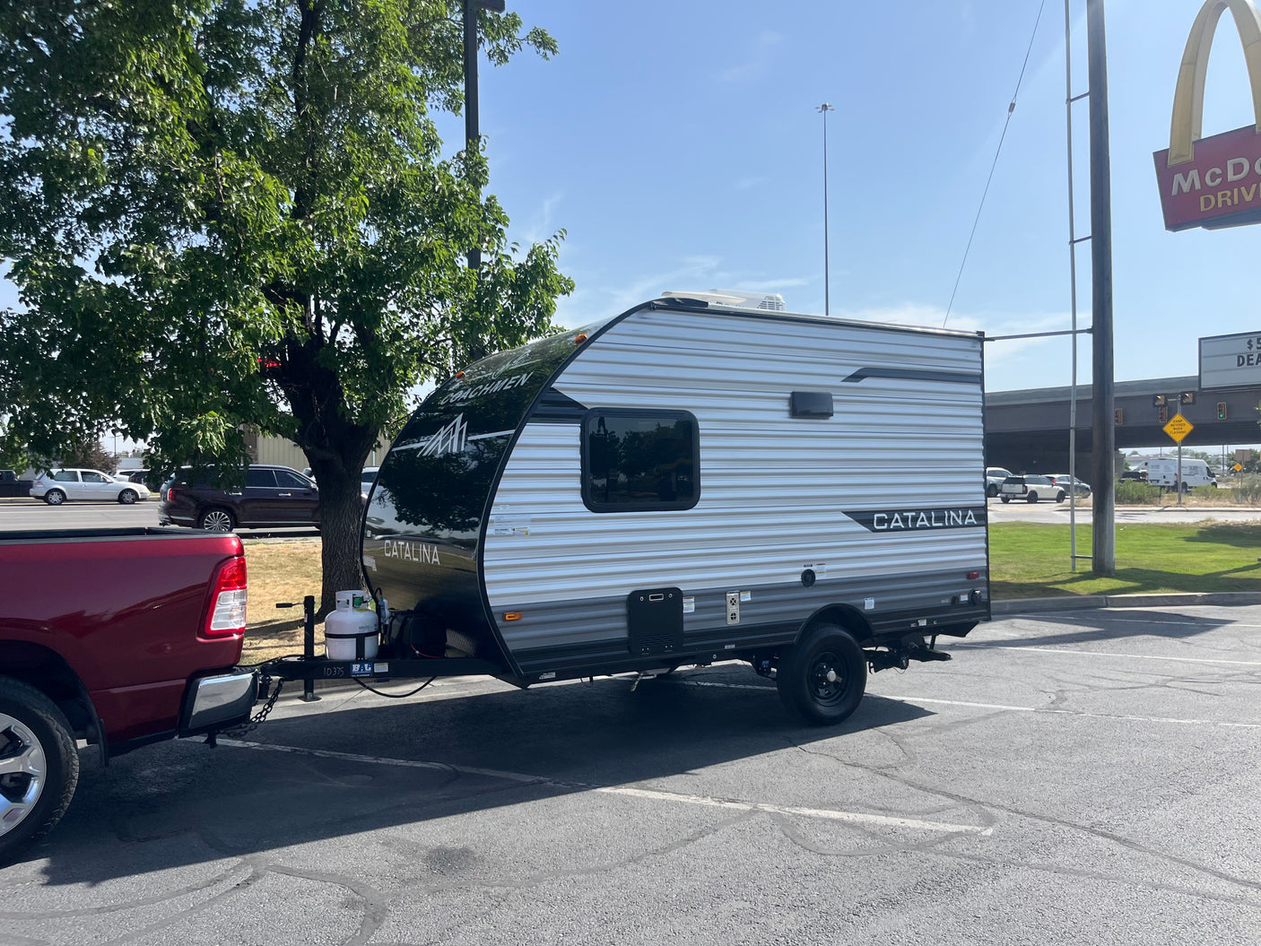 A red pickup tows a Coachmen Catalina RV rental in a parking lot, near a McDonald's. Ready for a road trip!