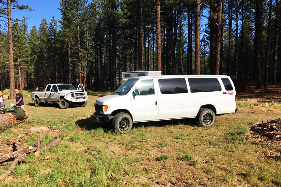 Adventure vehicles including an off-road van & camper in a forest clearing, perfect for your RV rental getaway.