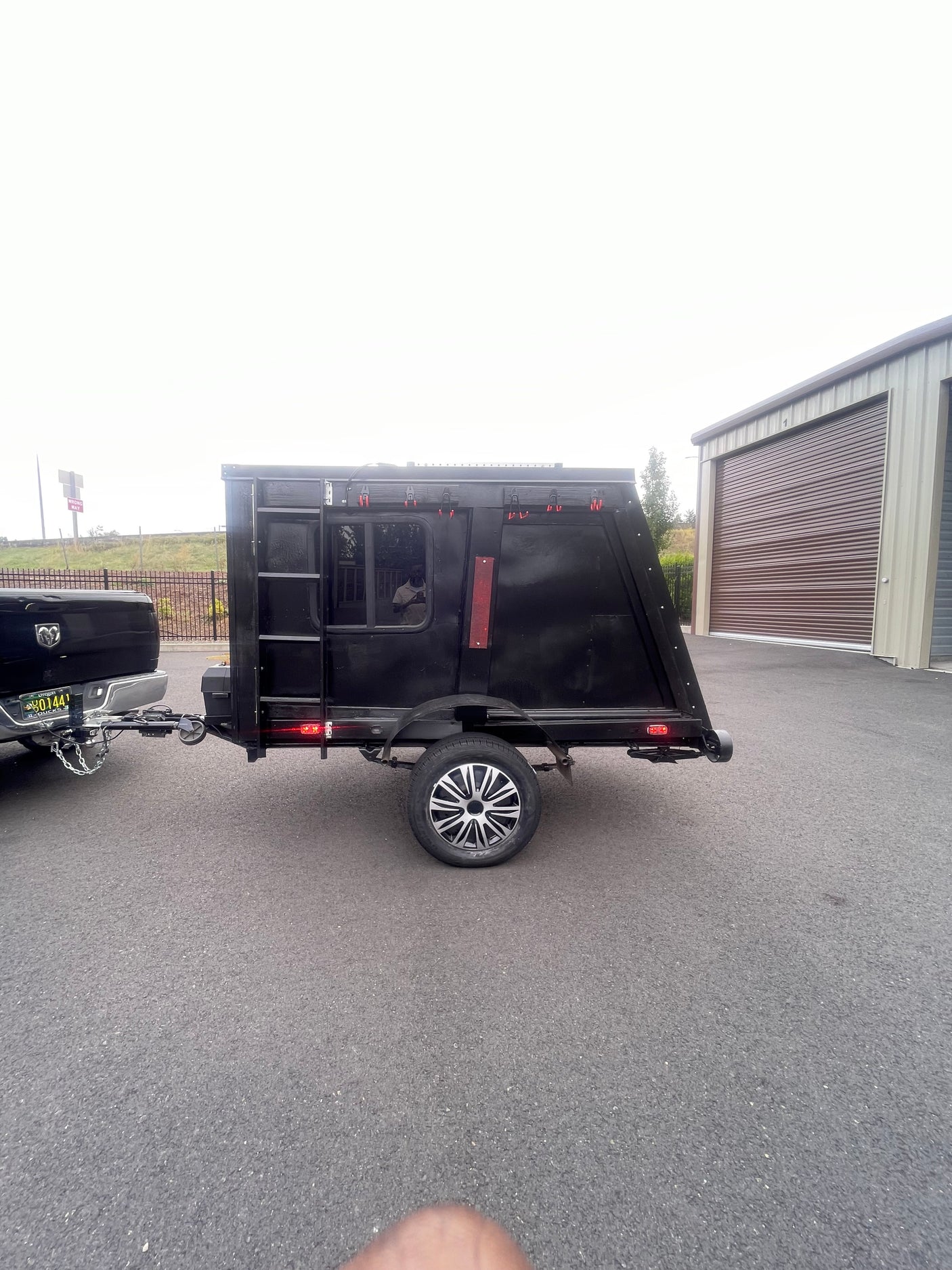 This custom black camper trailer, hitched to a truck, is perfect for an rv rental adventure, parked near storage units.