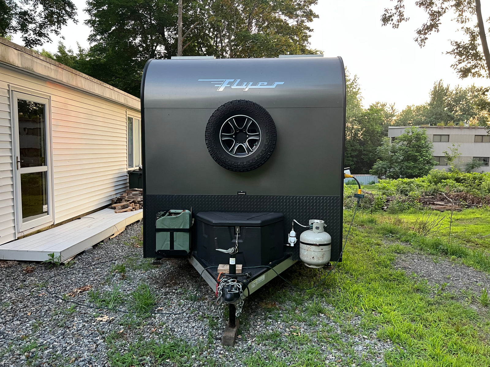 This sleek gray teardrop trailer, a perfect RV rental option, is set up for camping with its spare tire, propane, and power hookup.