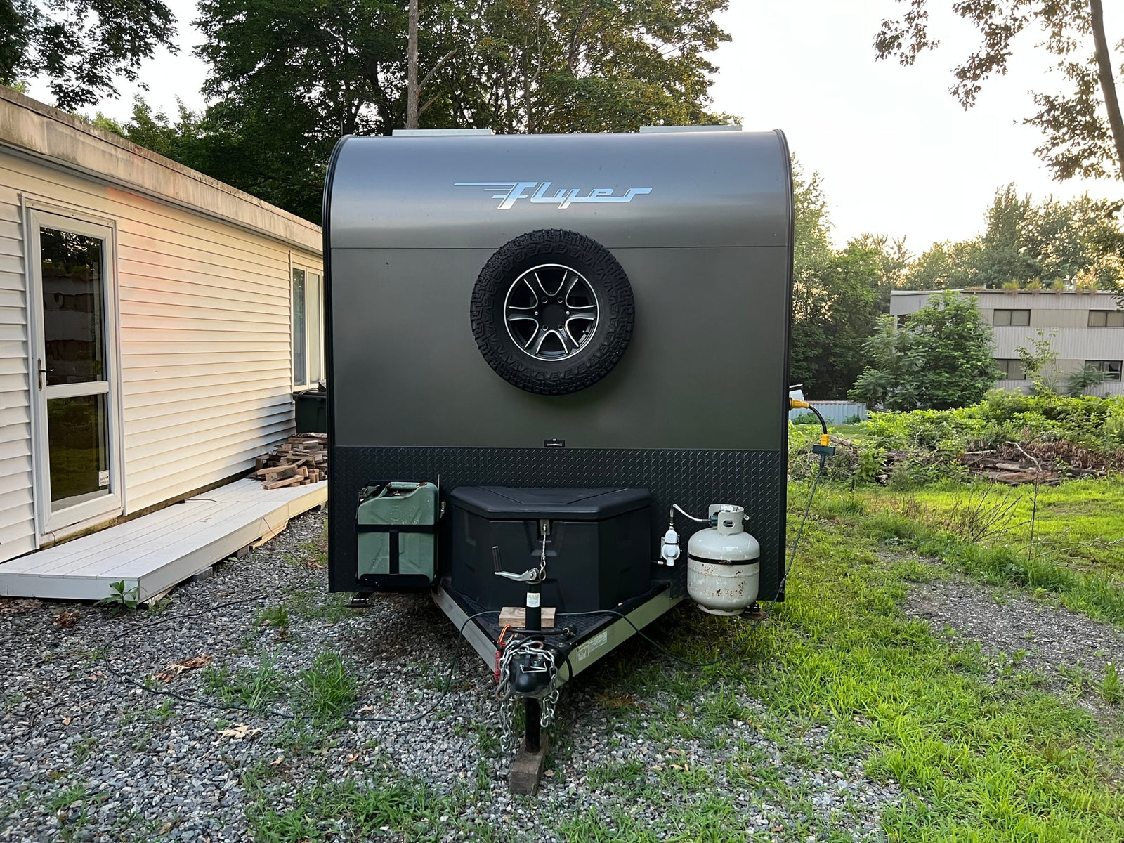 This sleek gray teardrop trailer, a perfect RV rental option, is set up for camping with its spare tire, propane, and power hookup.