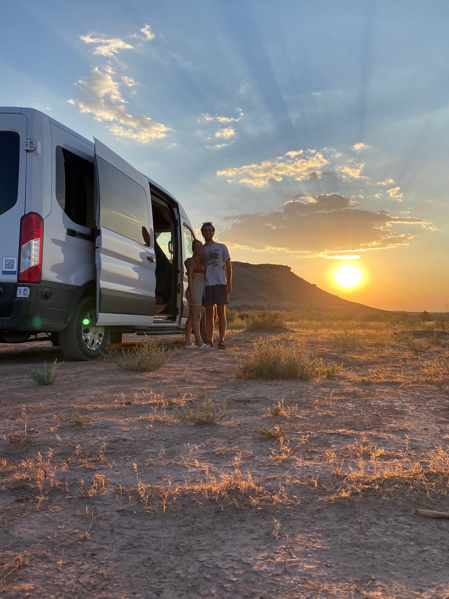 Couple enjoying a stunning desert sunset with their RV rental camper van.