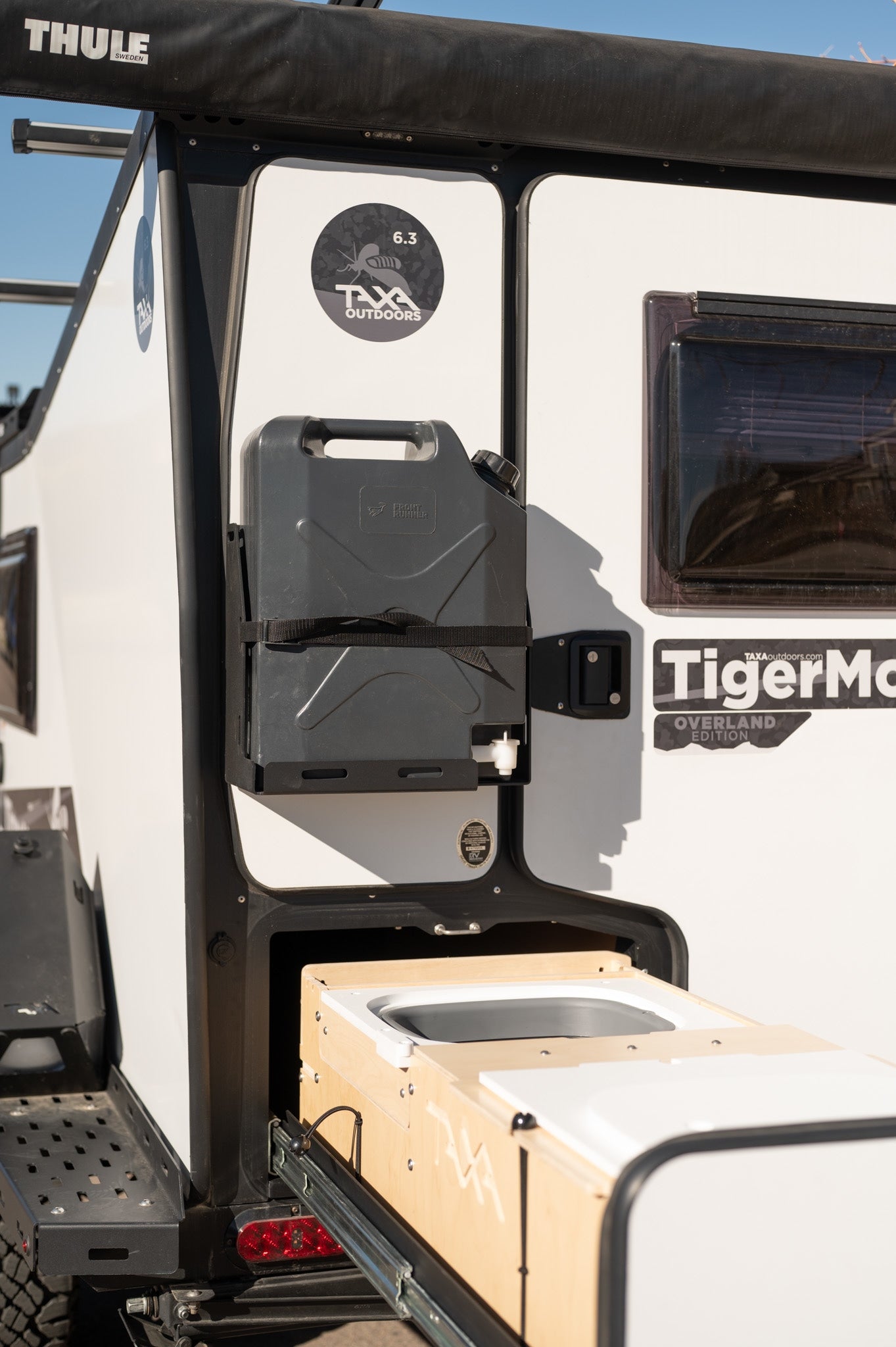 Side view of a white RV rental with a mounted water tank and a pull-out kitchen, ideal for outdoor trips.