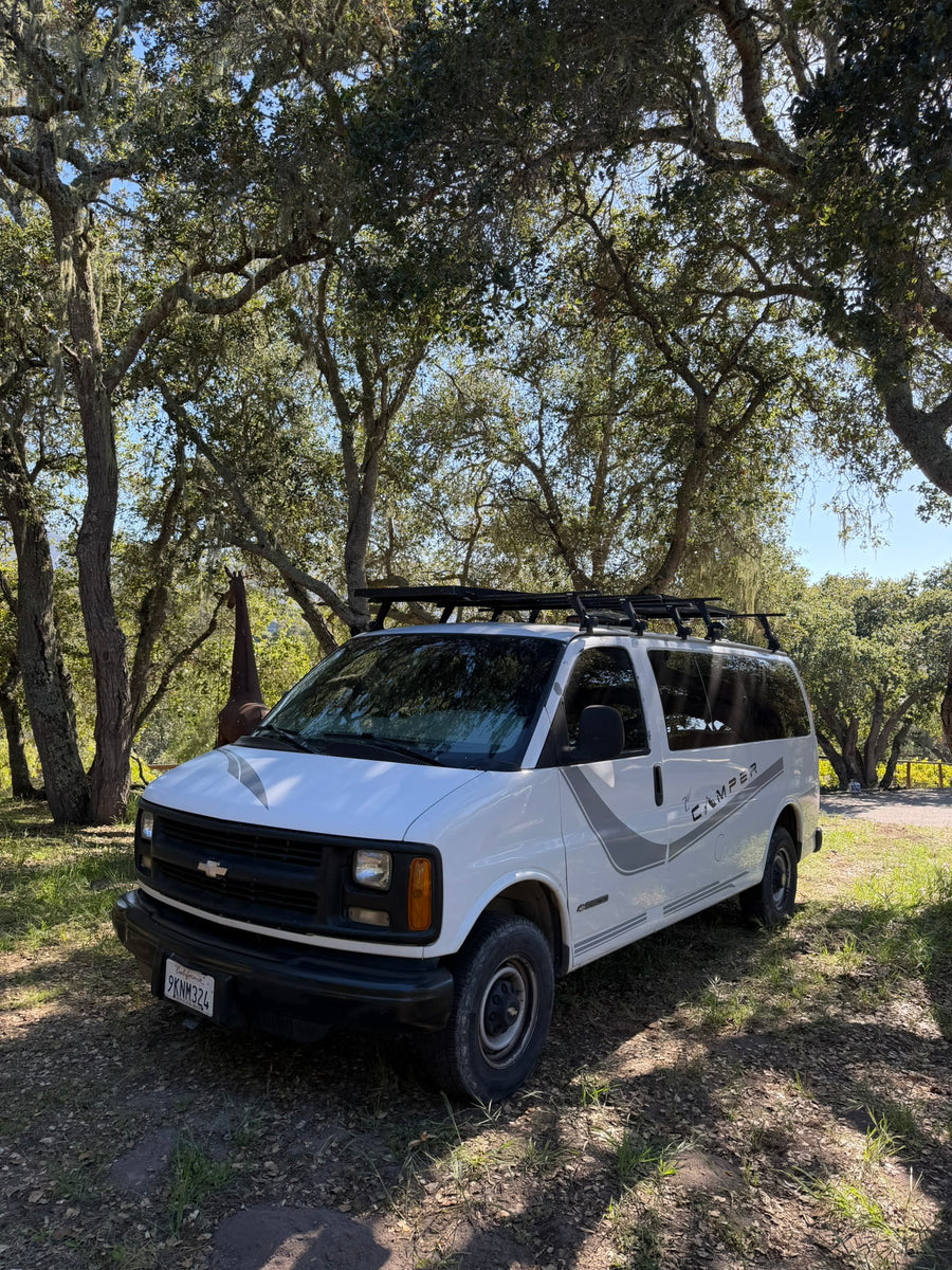 White Chevy camper van, great for an rv rental, parked under mossy oak trees with a giraffe statue in background.