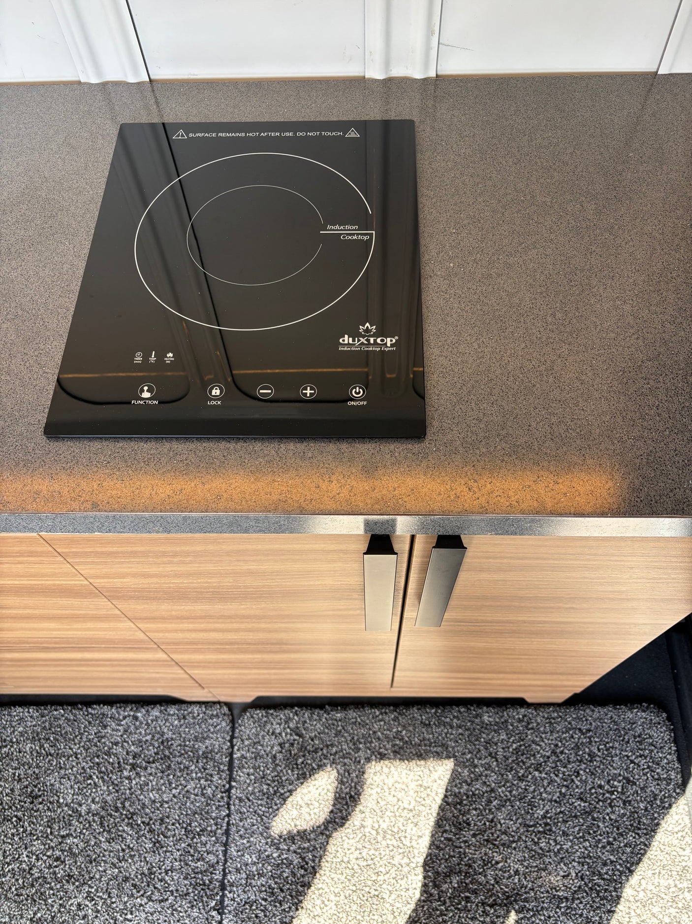 Top-down view of an RV rental kitchen showing a modern duxTop induction cooktop on a gray speckled counter.
