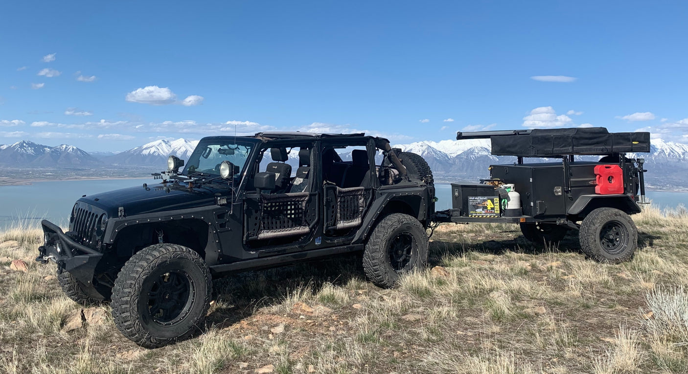Rugged black off-road Jeep towing an overlanding trailer with rooftop tent. Ideal **rv rental** for mountain adventures & scenic lake views.