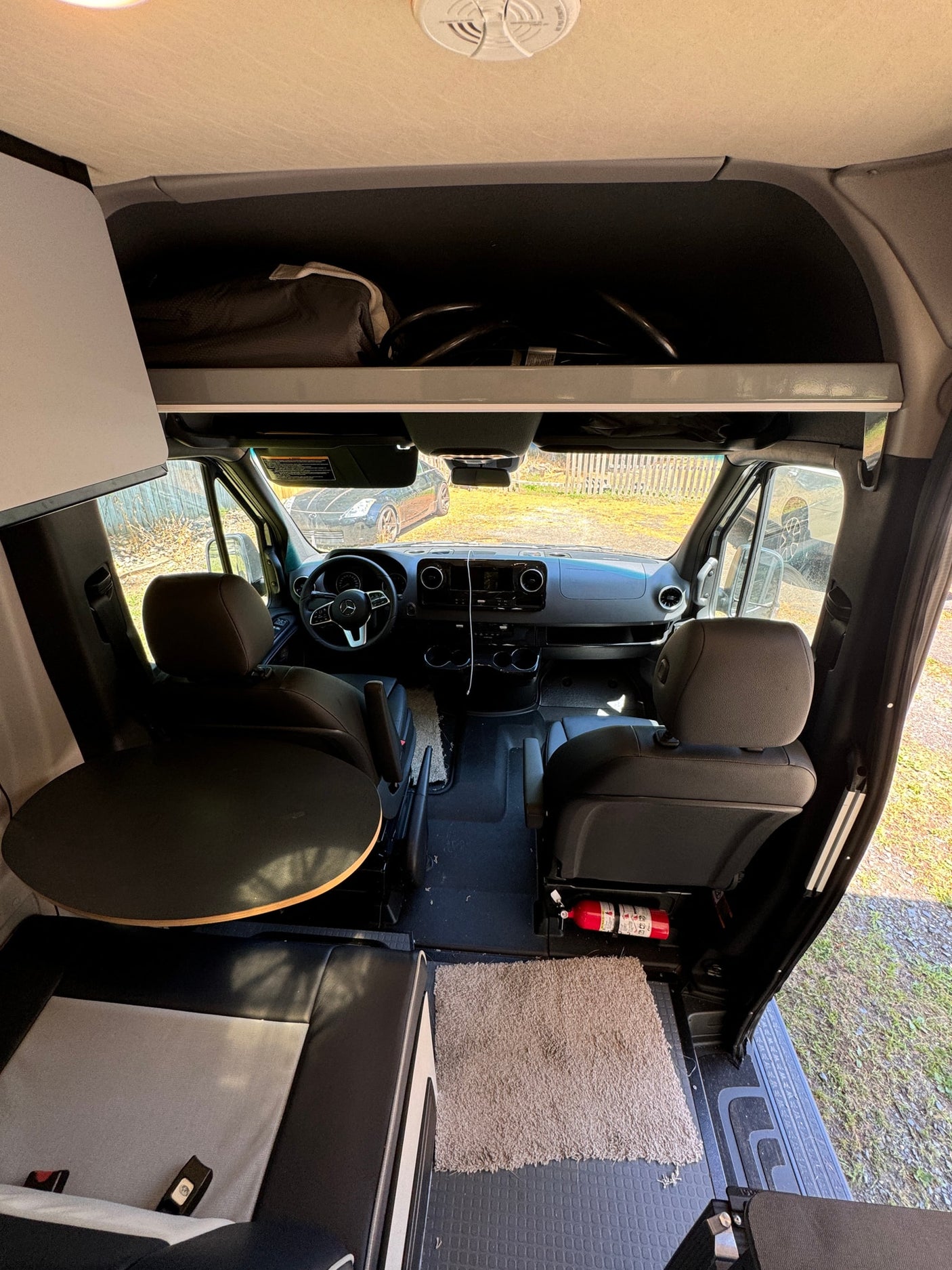 Wide-angle view inside an RV rental, featuring the driver's cockpit, front seats, and a rear dining table.