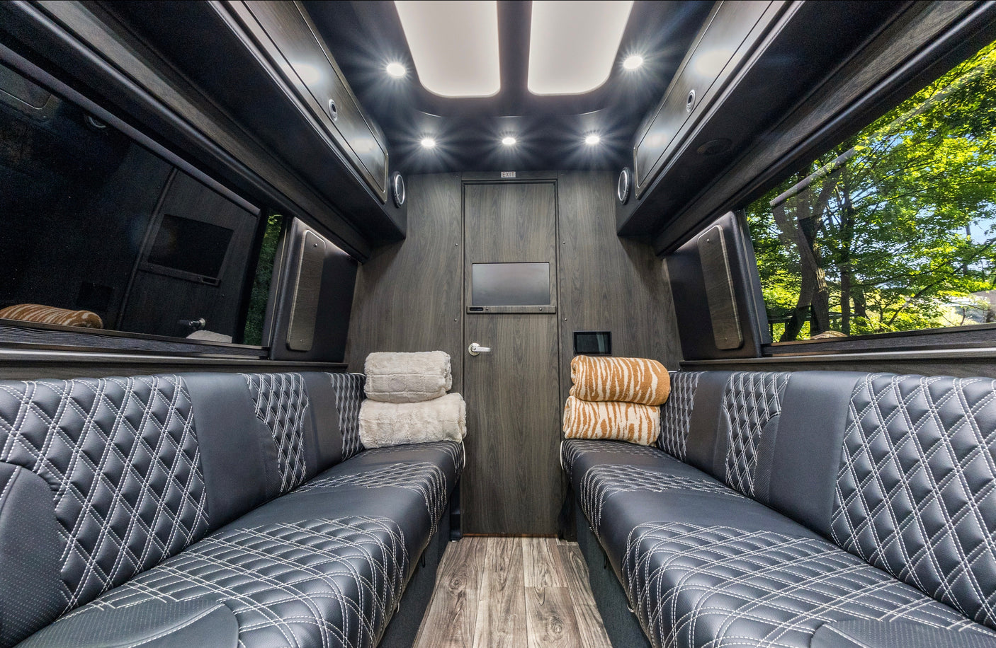Premium RV rental interior featuring black diamond-stitched seating, wood paneling, and bright cabin lighting.