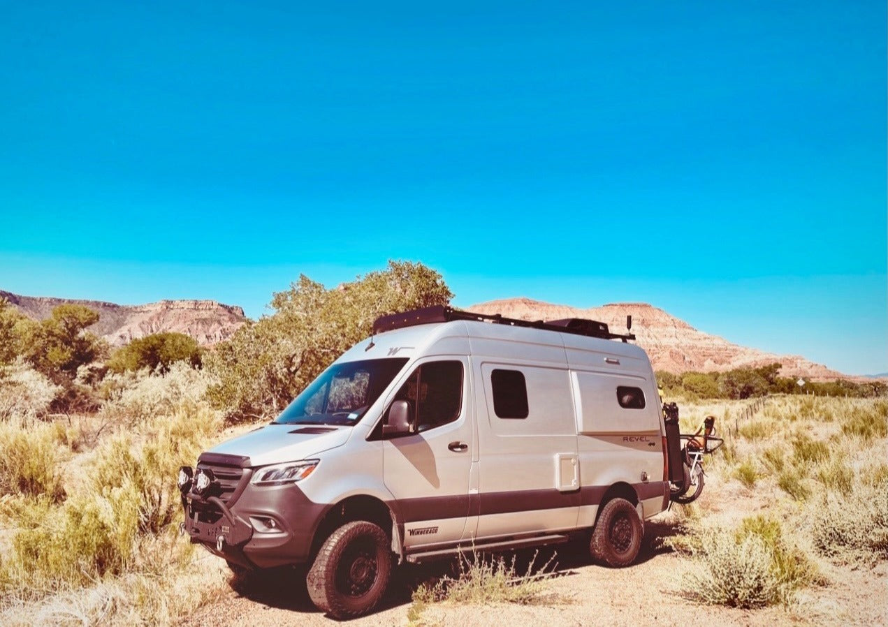 Silver Winnebago Revel camper van in a desert landscape with mountains, ideal for an rv rental adventure.