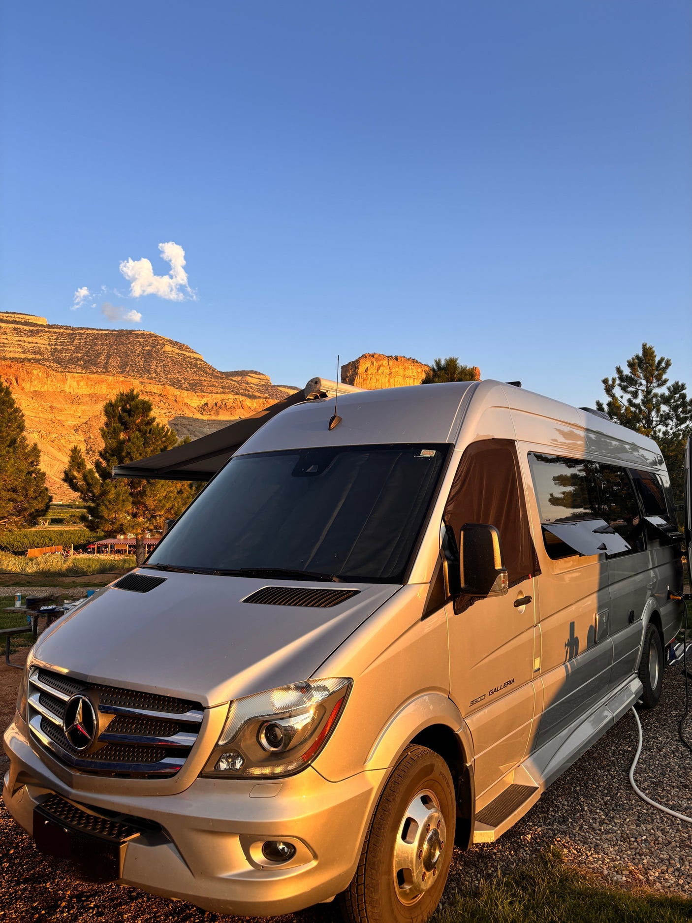 Golden light illuminates a Mercedes Sprinter rv rental parked with an awning extended, backed by orange desert mountains.