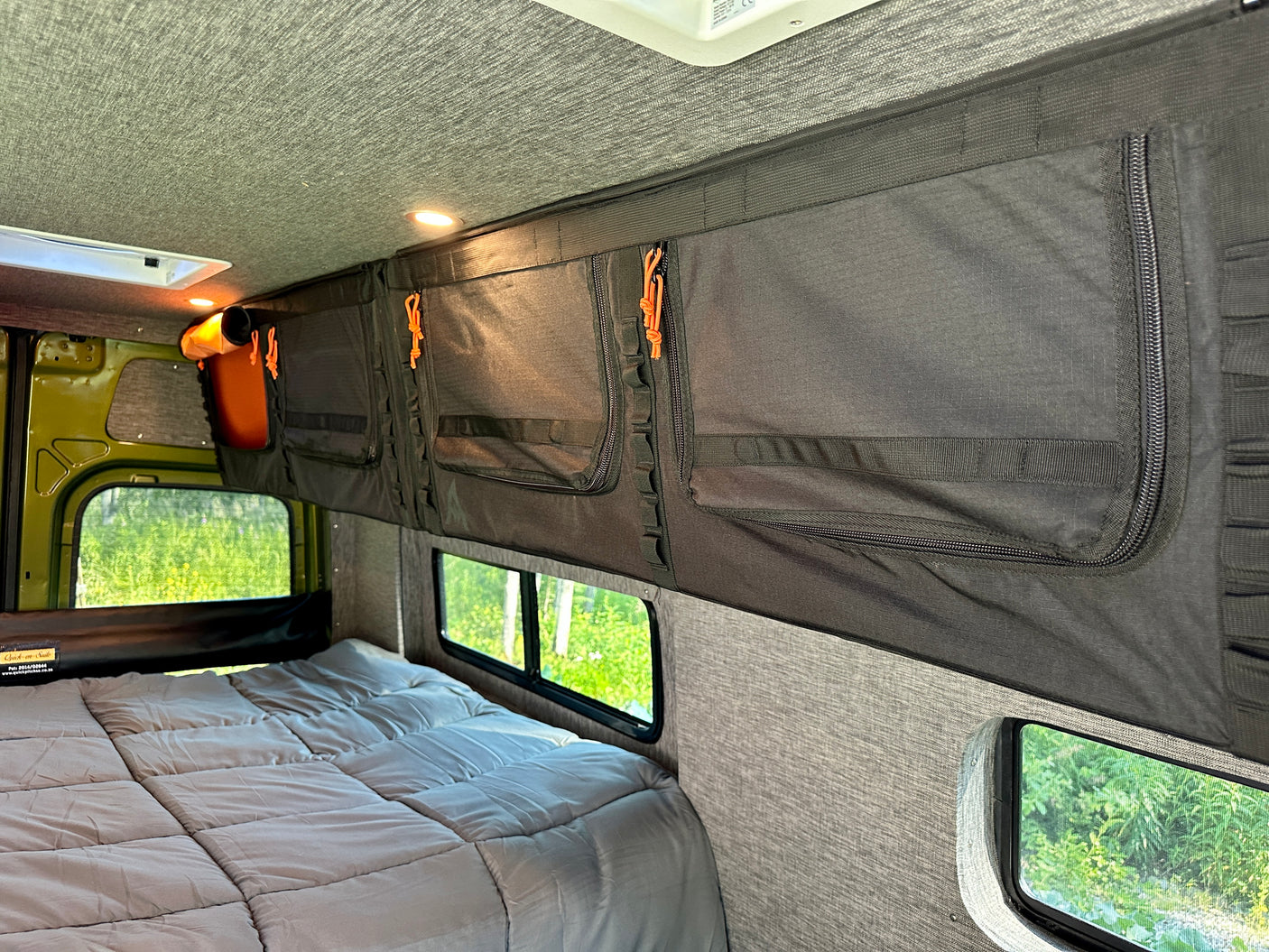Cozy RV rental interior with a comfy bed, organized storage pockets, and large windows showing lush nature.