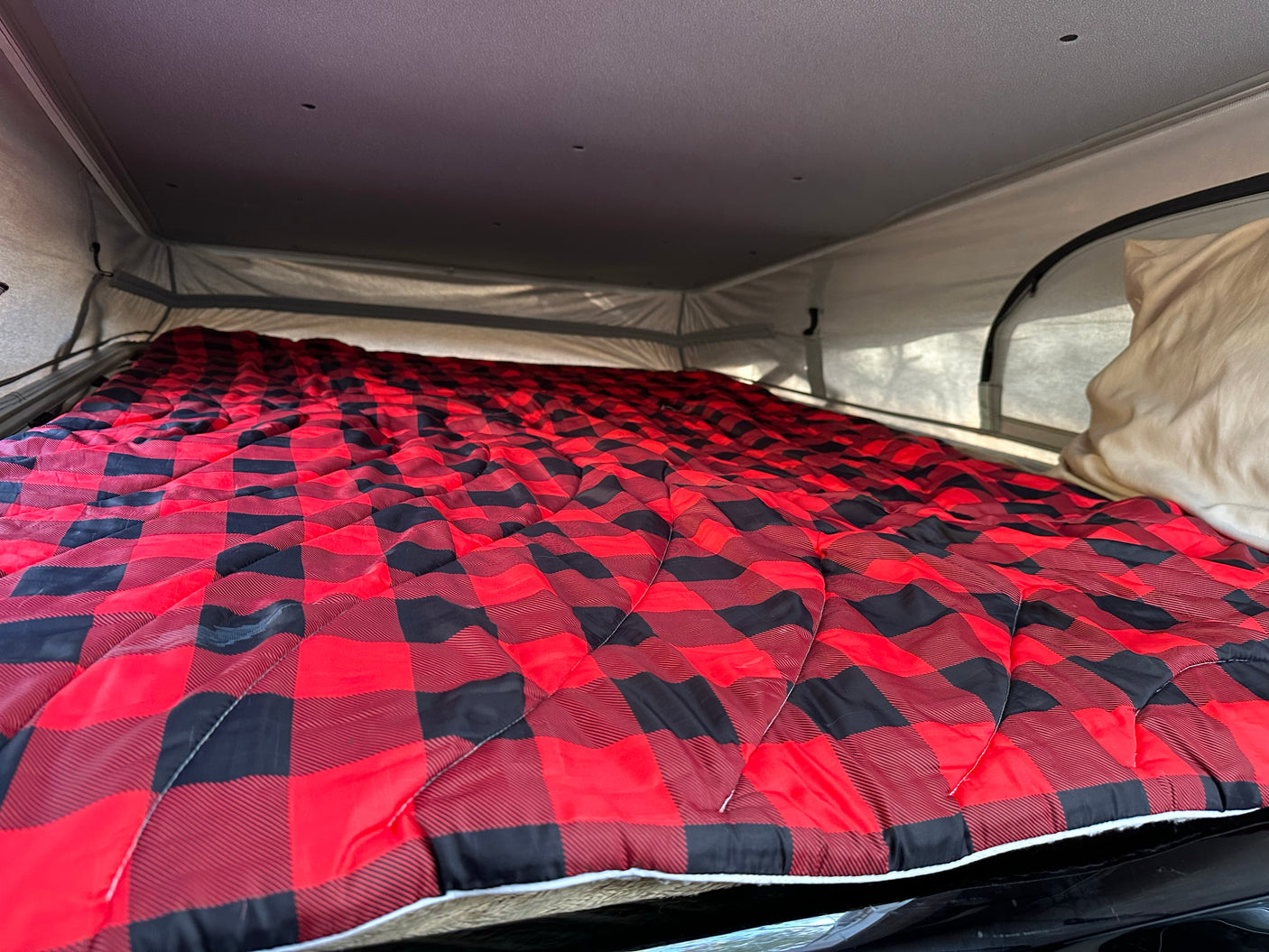 Cozy RV rental sleeping area with a vibrant red and black buffalo plaid comforter, ideal for comfortable camping trips.