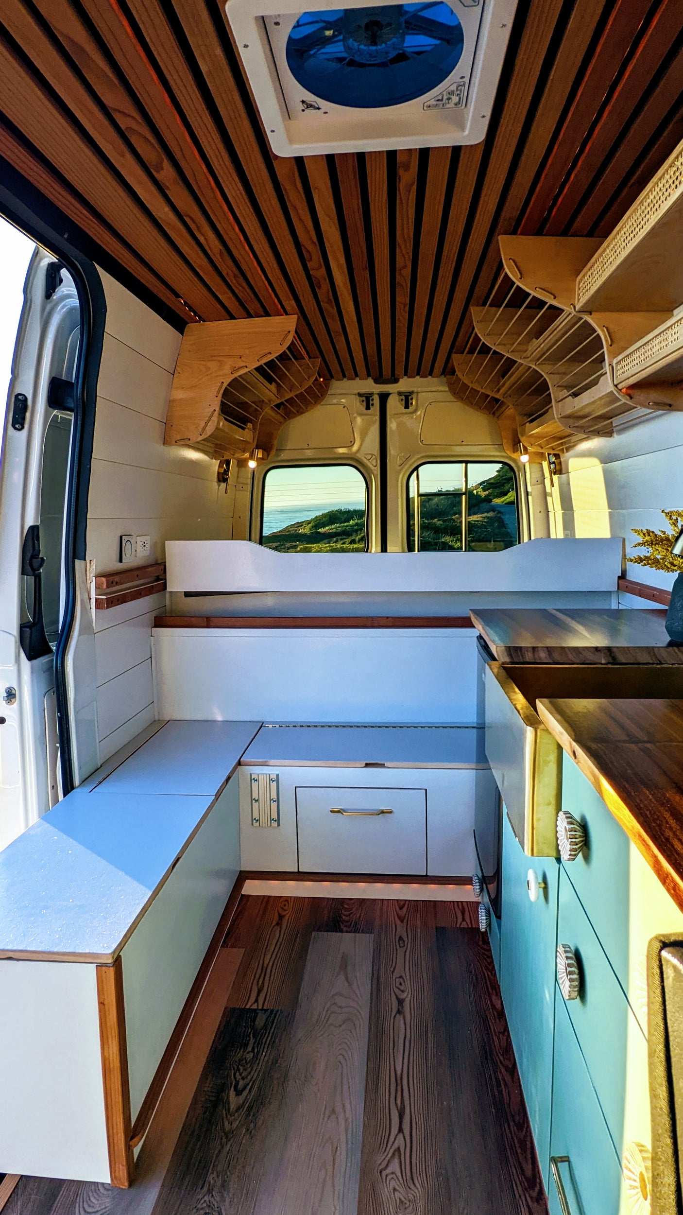 This RV rental interior boasts a warm wood ceiling, versatile seating, and a compact kitchen area with ocean views.