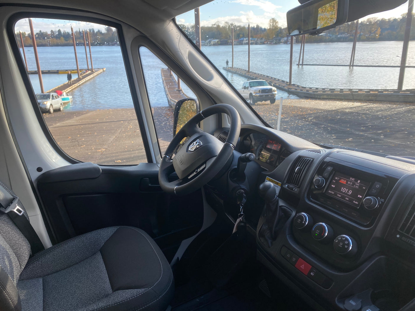 Interior of an RV rental van, looking out at a boat ramp with vehicles and docks extending into the water.