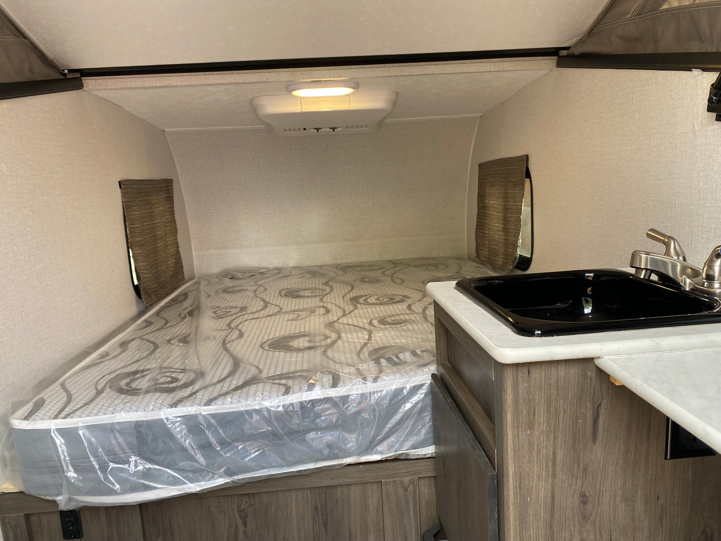 RV rental interior featuring a compact sleeping area with a mattress, a small kitchen sink, and overhead lighting.