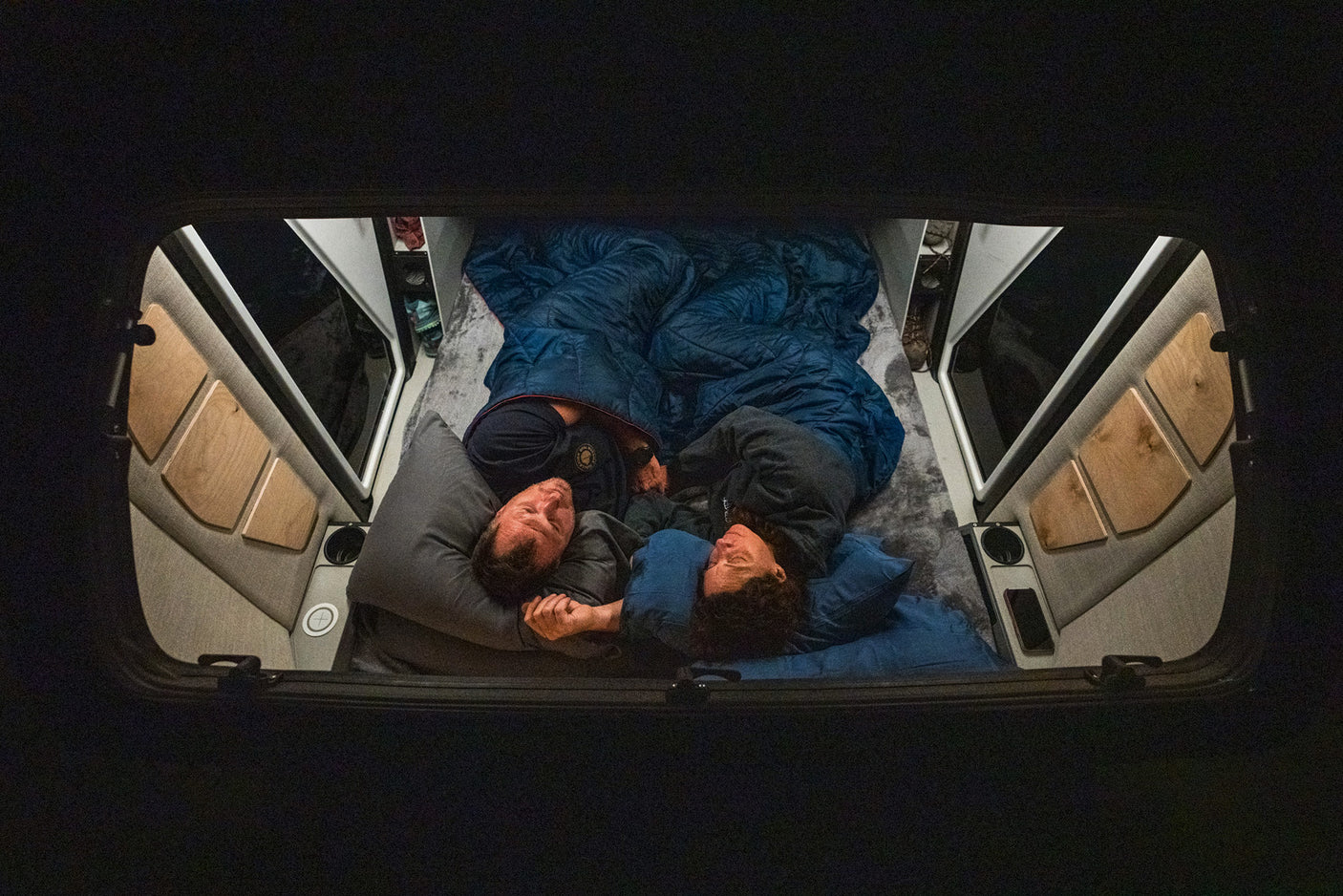 Overhead view: A couple sleeps soundly on a cozy bed inside their RV rental, showcasing the comfortable camper van interior.