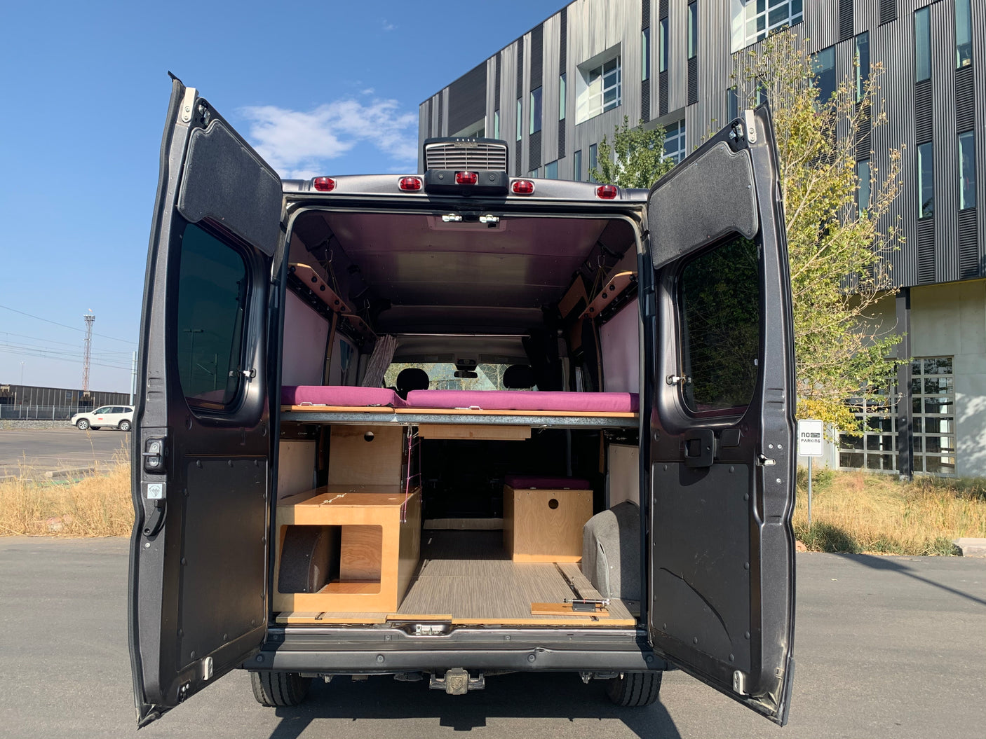 Discover this custom-built RV rental. Its open rear doors display a thoughtfully designed camper van interior with bed & storage.