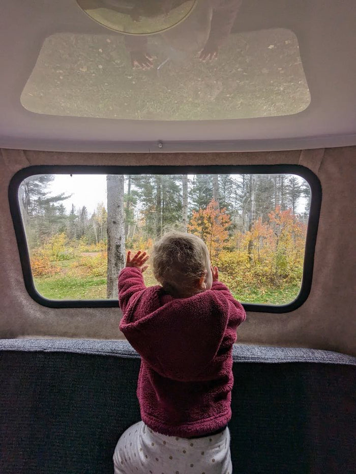 a small kitchen with a stove and kettle.|Compact RV rental interior featuring bunk bed