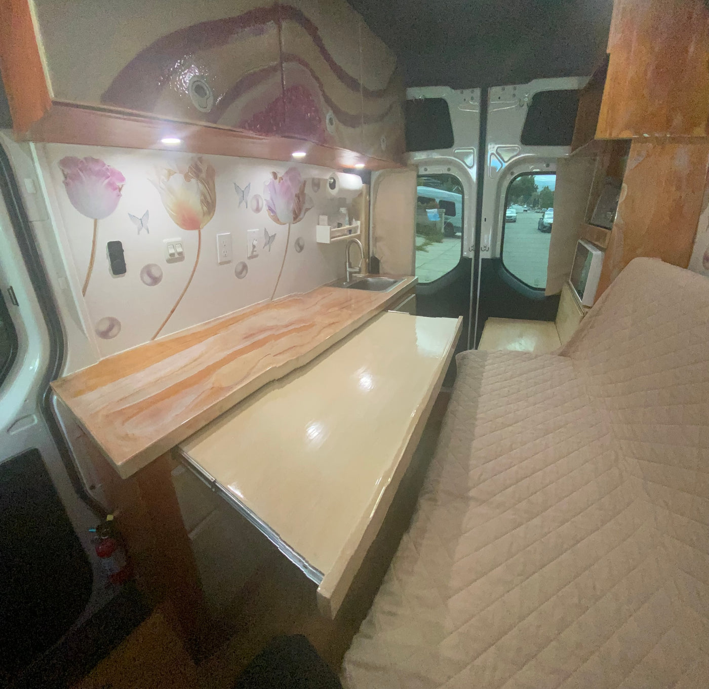 RV rental interior: A bright camper van living space with kitchen, pull-out counter, and comfortable quilted bed. — photo 10