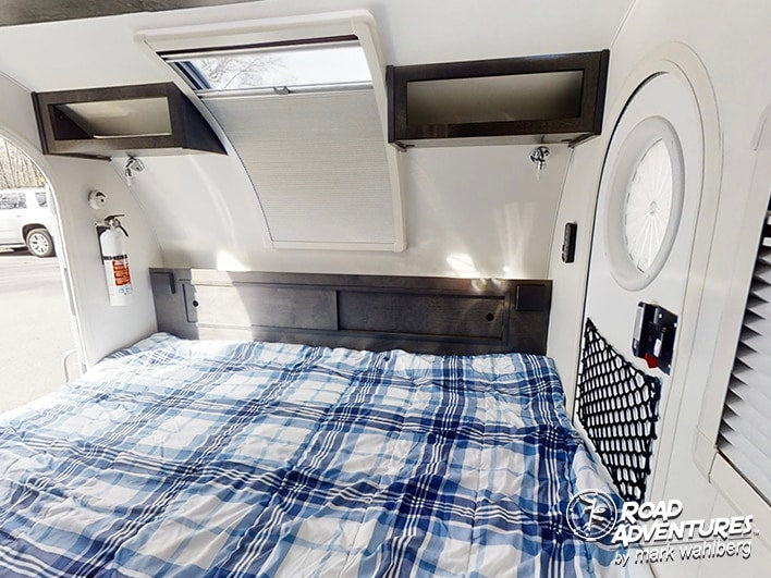 Inside an RV rental: a comfy bed with plaid comforter, storage, skylight, and fire extinguisher.