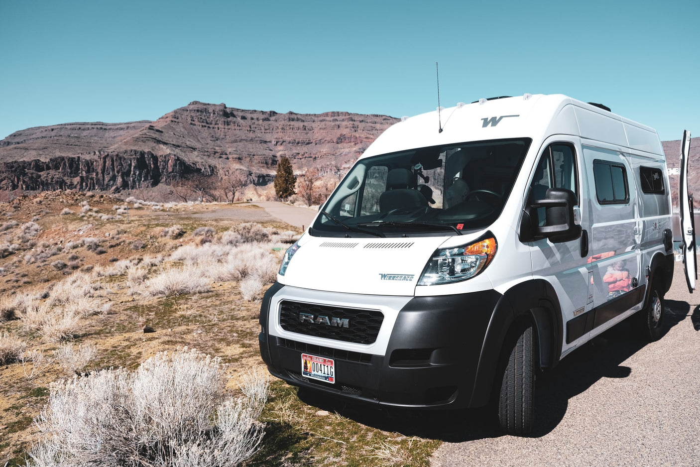 A white Winnebago Solis Ram ProMaster camper van rv rental is parked roadside with arid landscapes and layered mountains beyond.